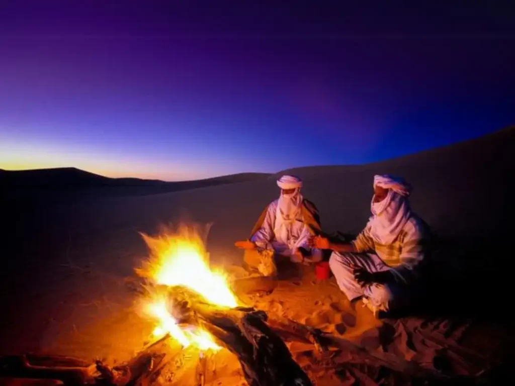 Group of people gathered around a fire during sunset in the desert.